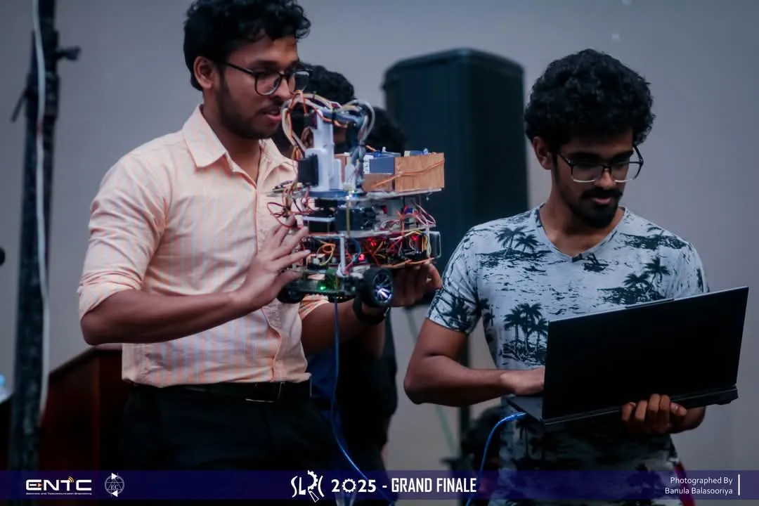 Two team members on the competition floor, one holding the robot while the other works at a laptop.